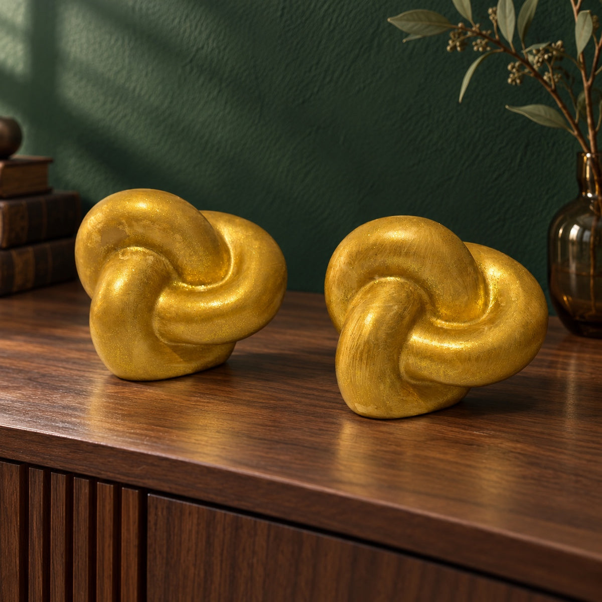 Set de 2 esculturas decorativas de nudo doradas sobre una cómoda de madera